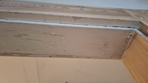 Zbliżenie na narożnik drewnianej futryny z trudnymi do usunięcia warstwami farby